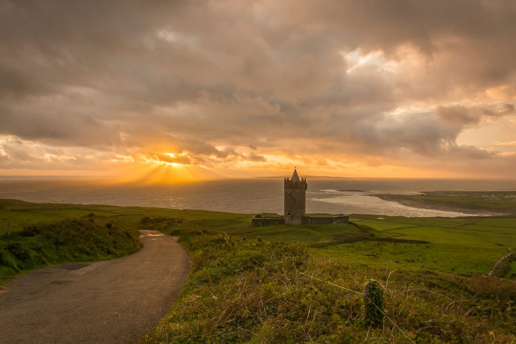The low evening sun breaking through cloud over the Atlantic with Doonagore castle in the foreground