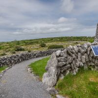 The path leading around the fort with a stone wall on the left and the wall of the fort on the right. Burren fields outside the wall.