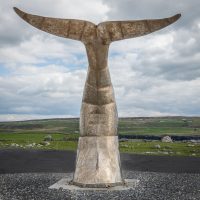 Bronze monument of a dolphin's tail at the pier in Doolin. Green fields and hills behind