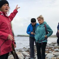 Oonagh talking to a group while foraging in County Clare on the rocks. Clare coastline in the background